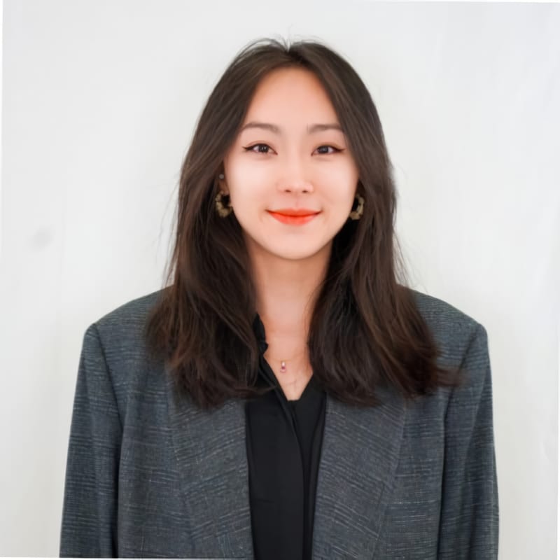 Smiling Asian woman with long dark hair, wearing a grey blazer and hoop earrings.