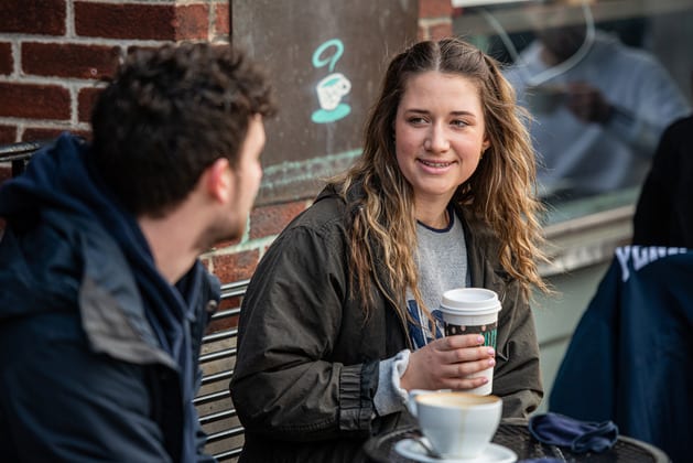Smiling woman holding coffee talks to man at outdoor cafe.
