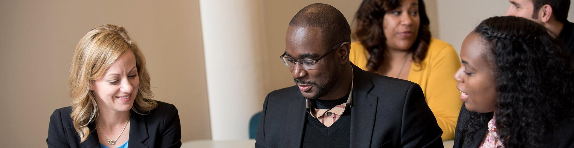 Diverse group of four individuals collaborating and discussing in a professional or academic setting.