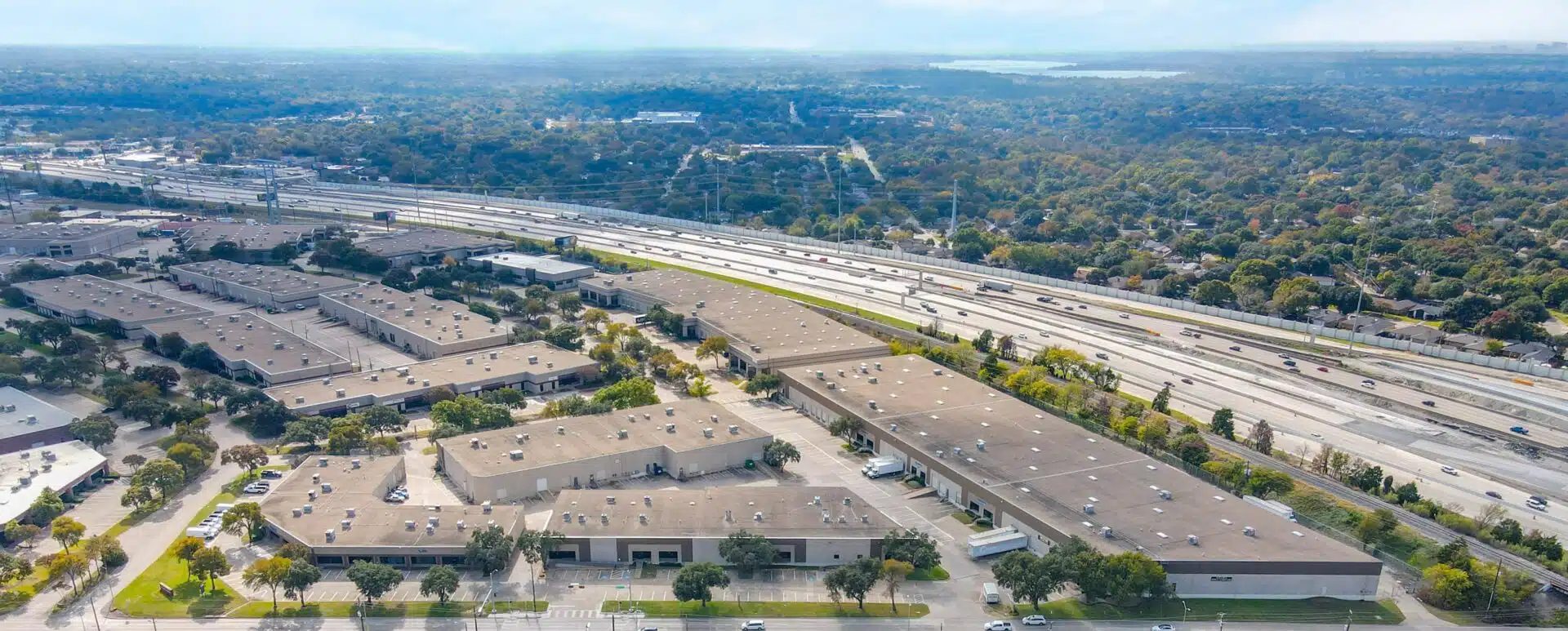 Aerial view of an industrial park, multi-lane highway, wooded landscape, and distant lake.