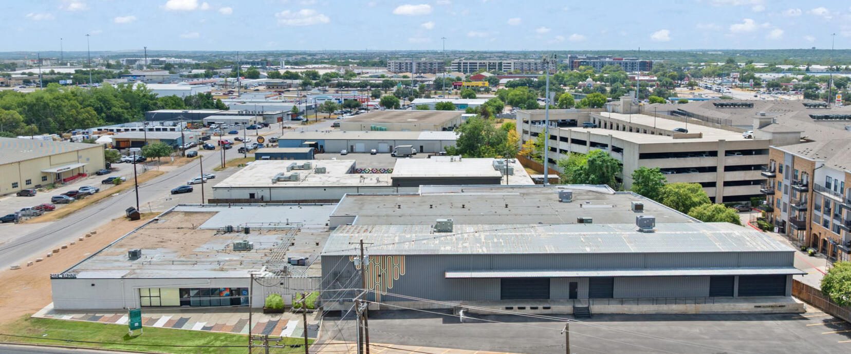 Aerial view of an urban industrial area with warehouses, a parking garage, apartment buildings, and roads.