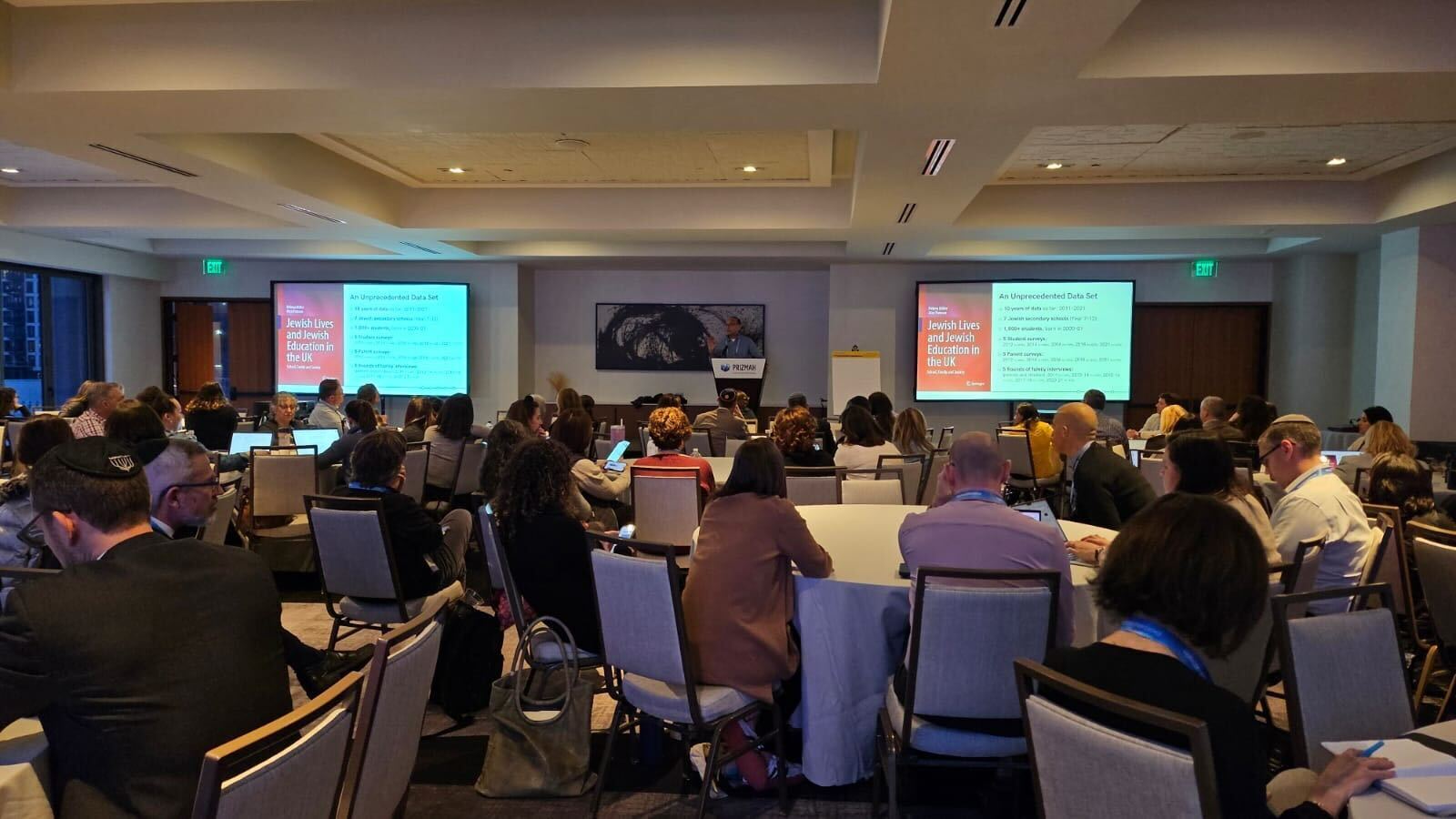 Attendees watch a presentation on Jewish education in a conference room.