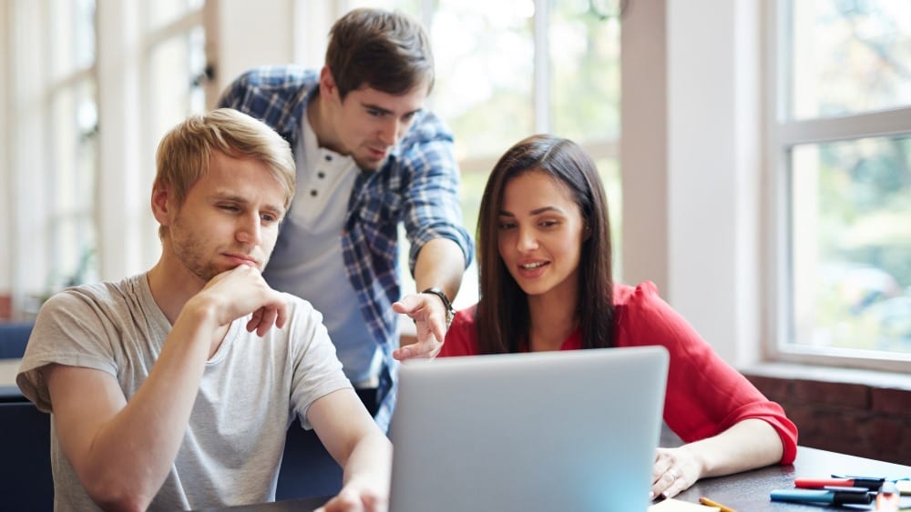 Three young people collaborating and looking at a laptop.