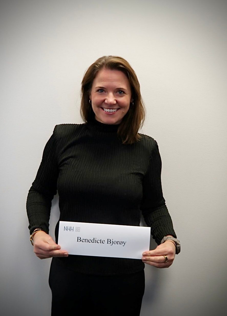 Benedicte Bjorøy smiling and holding a sign from NHH.