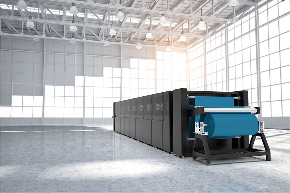 Large industrial machine with blue material roll in a modern, sunlit factory building.