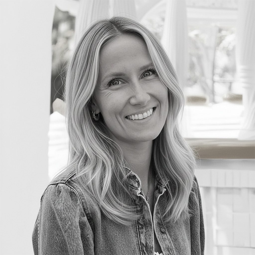 Black and white portrait of a smiling woman with long blonde hair wearing a denim shirt.