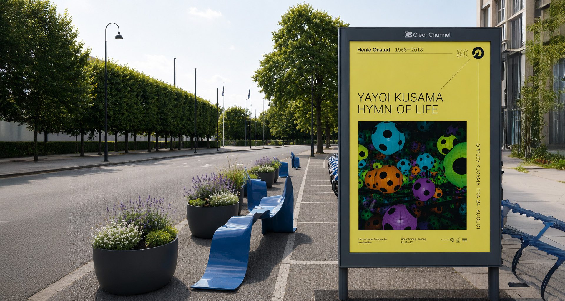 Billboard for Yayoi Kusama's 'Hymn of Life' exhibition, with colorful spheres, by a road with trees.