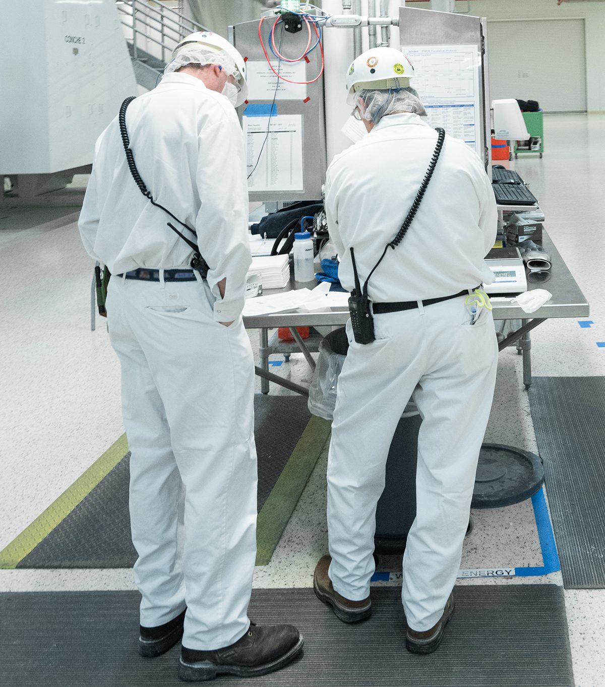 two factory workers wearing proper safety attire for company-owned two-way radios