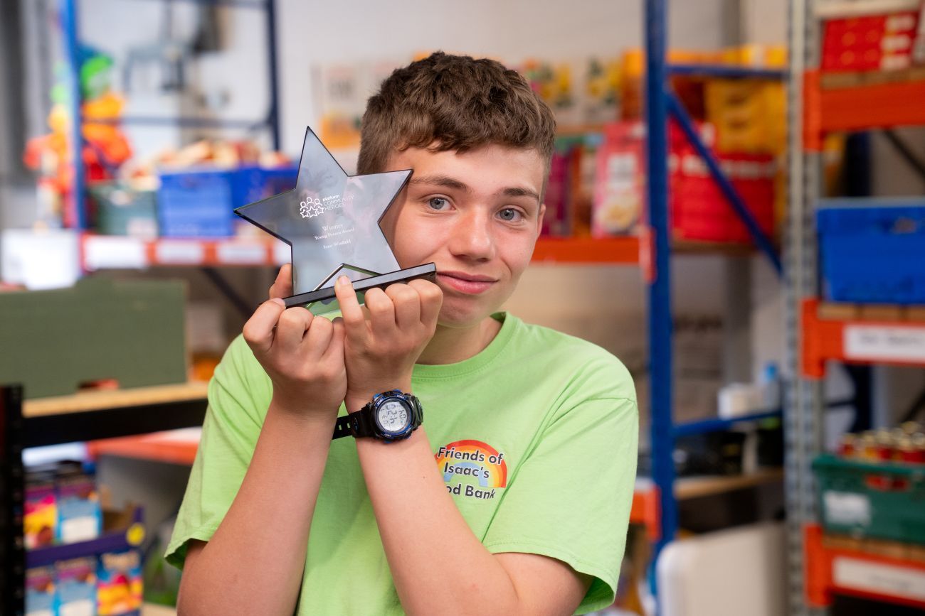 Young man in green shirt holding a star-shaped trophy, smiling in a food bank warehouse.