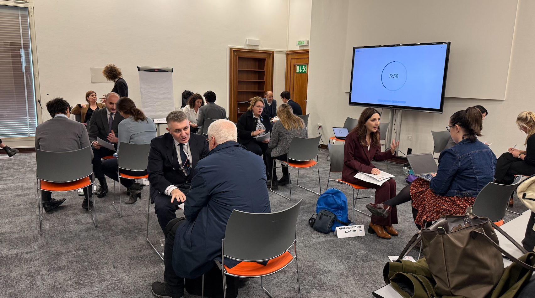 People engaging in discussions in small groups during a workshop, with a timer on a large screen.