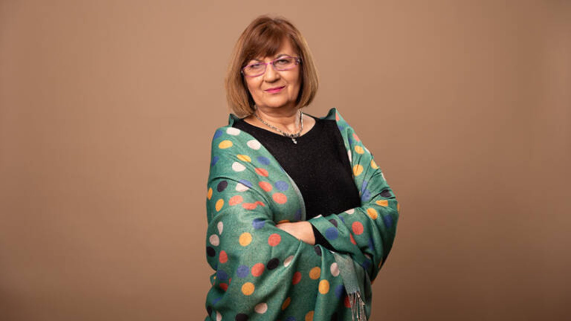 Woman with glasses and a green polka-dot shawl with colorful polka dots, arms crossed, smiling.