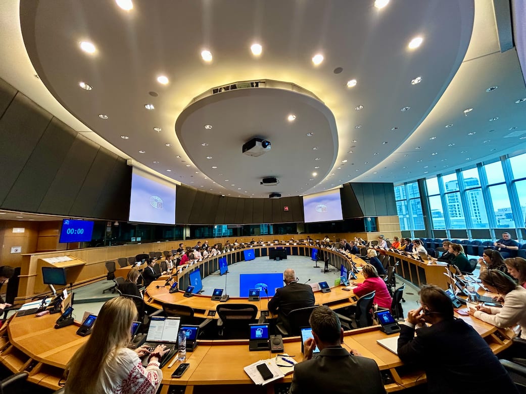 People attend a meeting in a spacious, modern conference room with a circular table and multiple screens.
