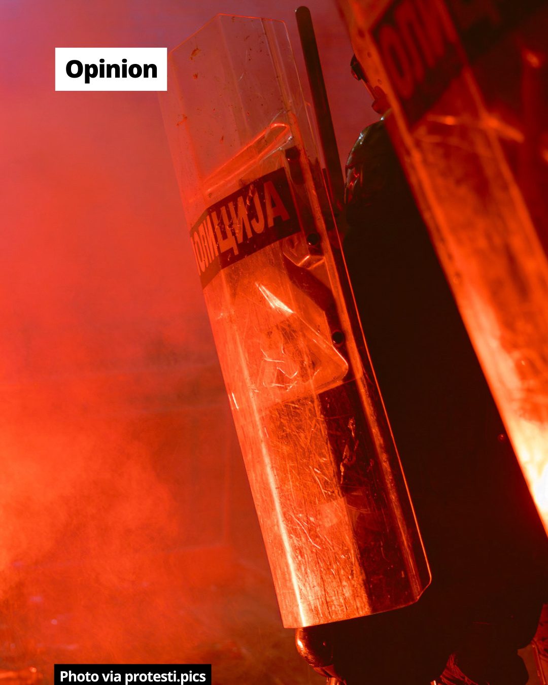 Riot police shields illuminated by intense red light or smoke, with Cyrillic text 'ПОЛИЦИЈА' visible.