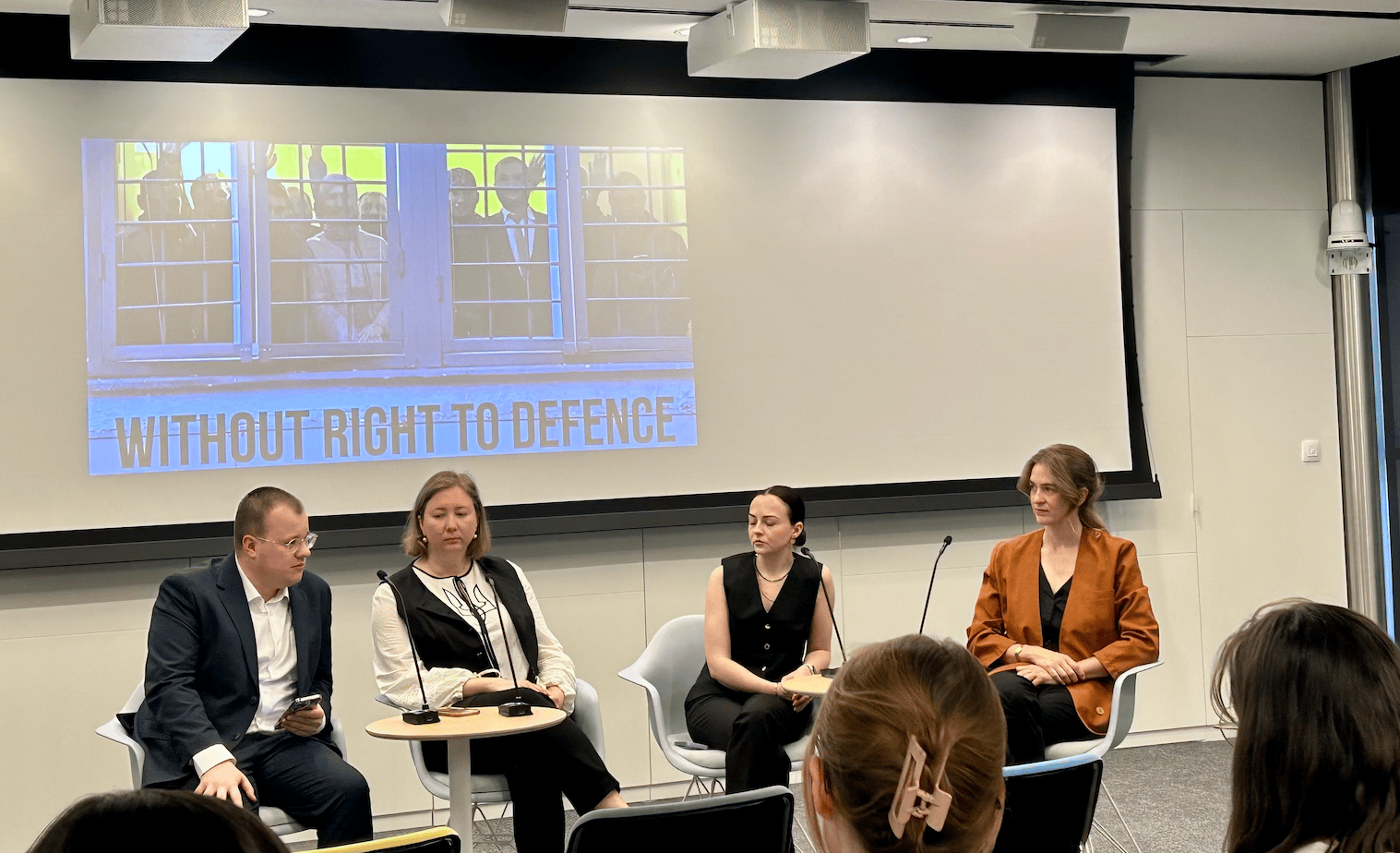 Panel discussion on 'Without Right to Defence' with four speakers and a screen.