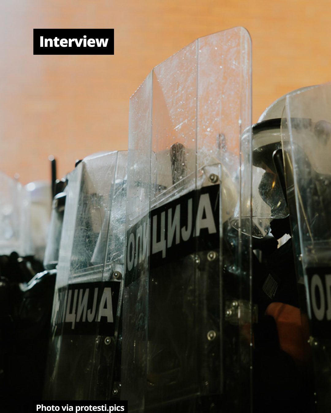 Riot police officers in protective gear with transparent shields featuring 'POLICIJA' text in Cyrillic.