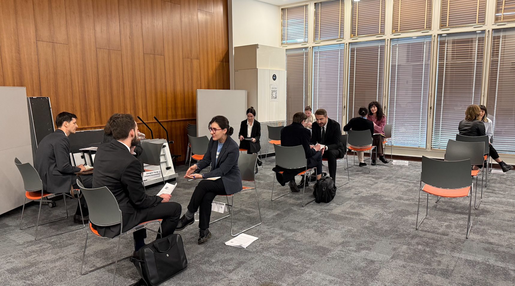 Professionals in suits networking and conversing in a conference room with wooden walls and large windows.