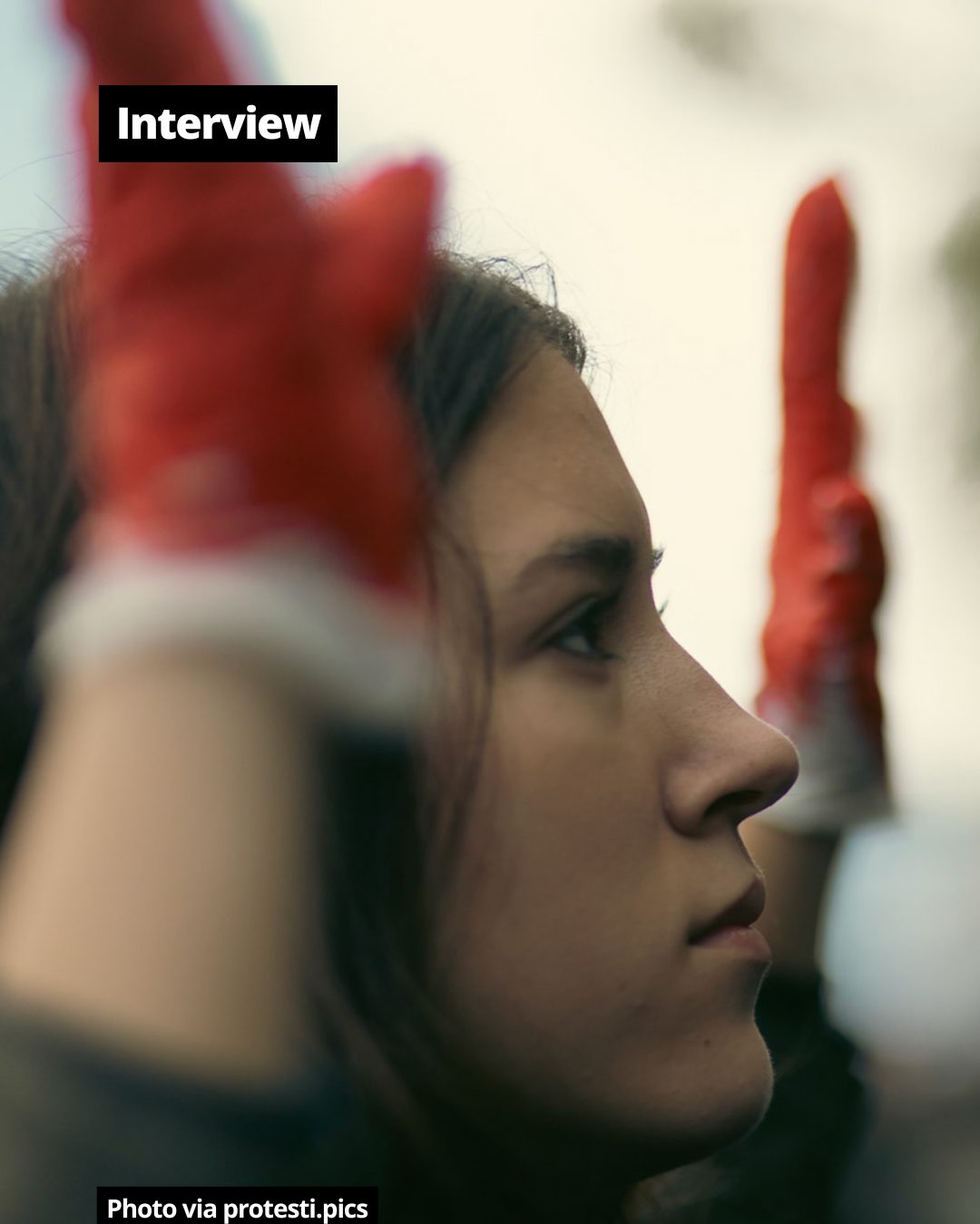 Profile of a young woman with a serious expression, with blurry red elements in the foreground and background.