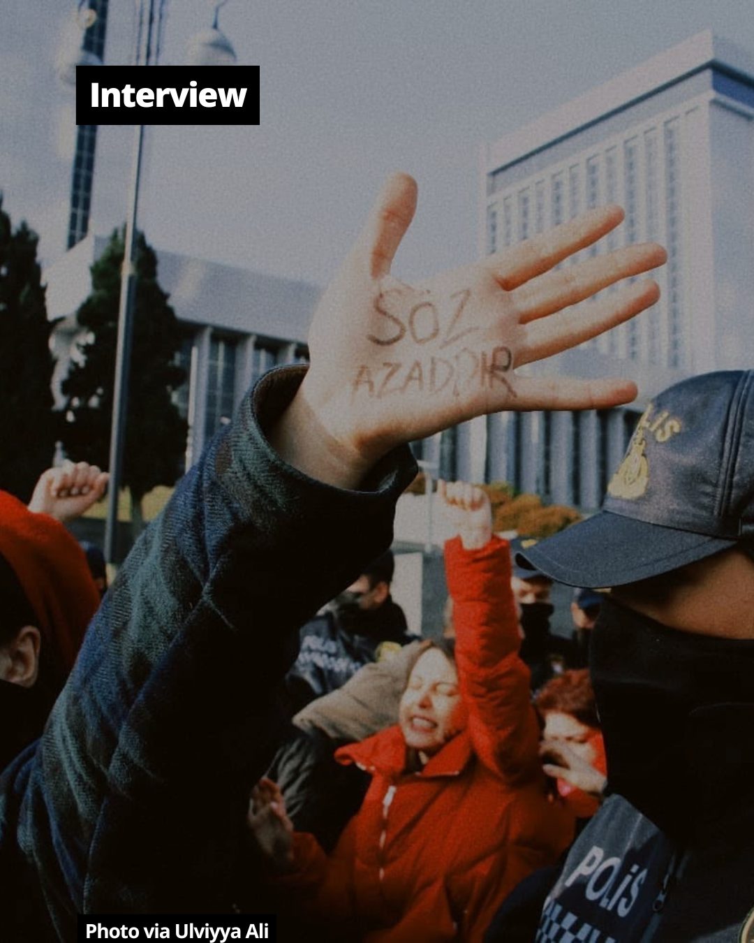 A hand at a protest with 'SÖZ AZADDIR' (Freedom of Speech) written on it, amidst other demonstrators.