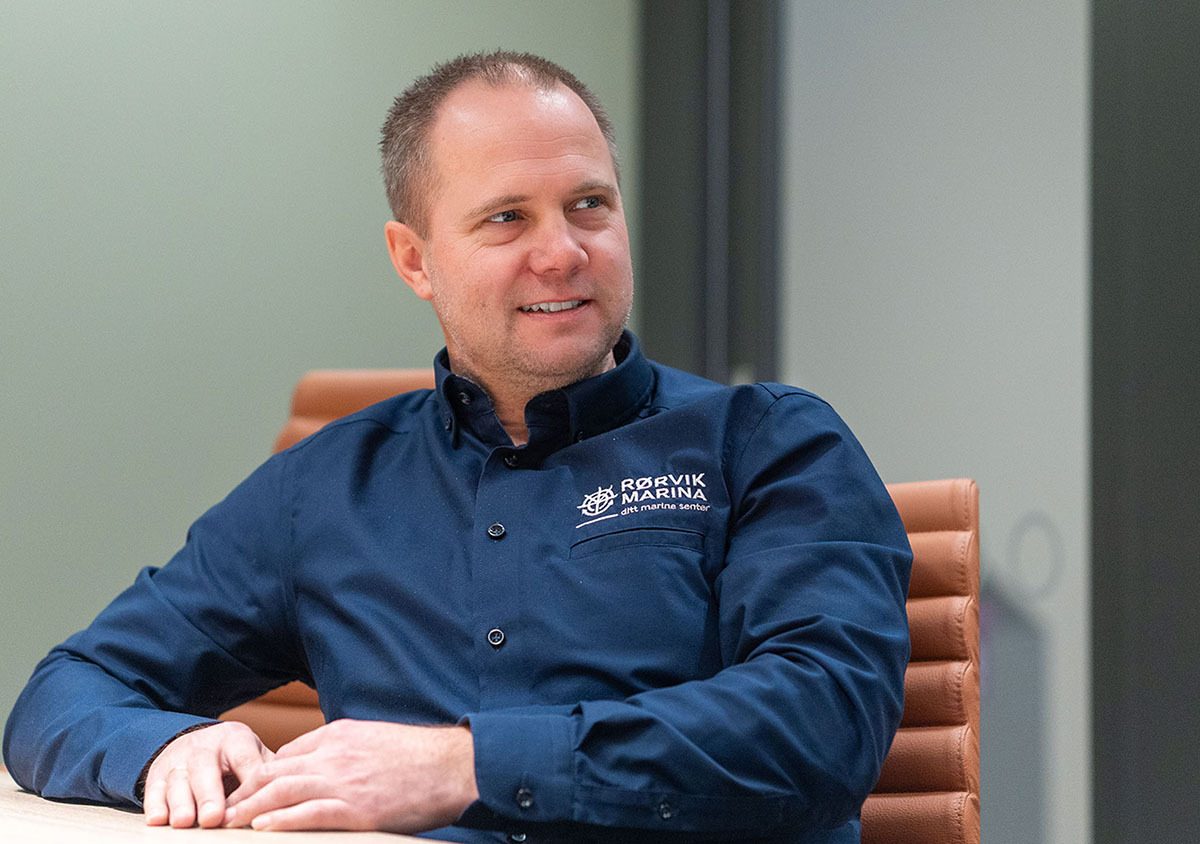 Smiling man in a blue shirt with a Rørvik Marina logo, looking to the side.