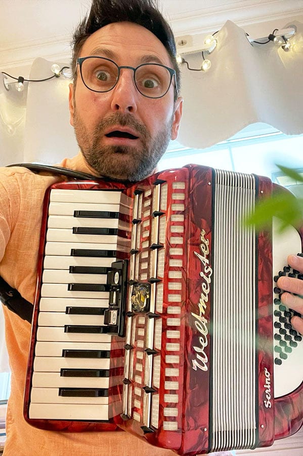 Shocked man with wide eyes and open mouth holding a red accordion.