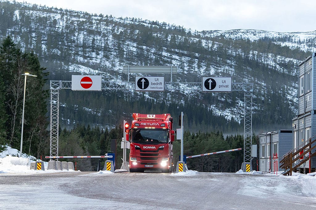 Red truck at a snowy road checkpoint with gates and signs in a winter landscape.