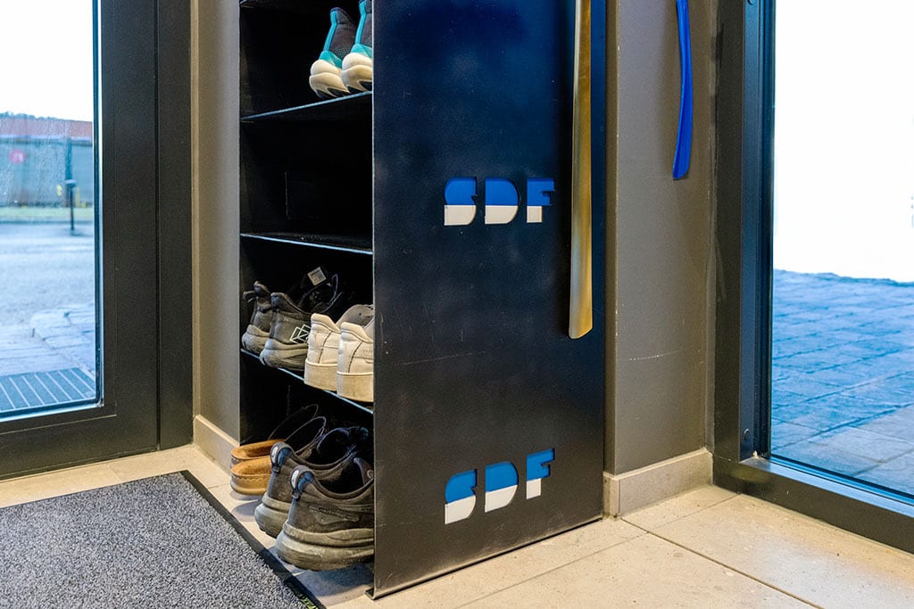 Black shoe rack with shoes and an SDF logo next to an entrance.