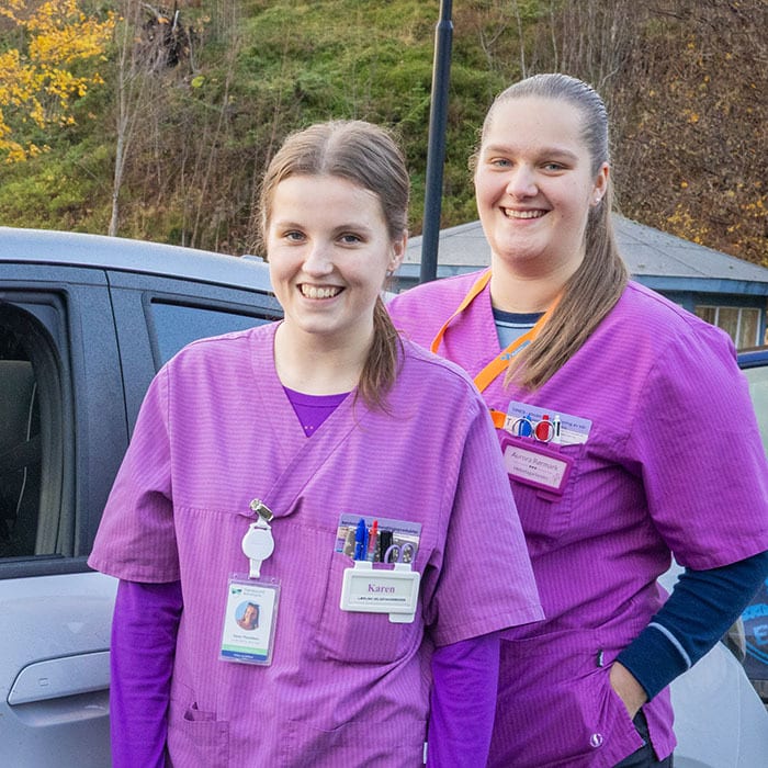 Two smiling healthcare workers in purple scrubs.