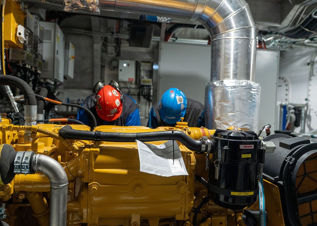 Two workers in hard hats working on heavy yellow machinery.