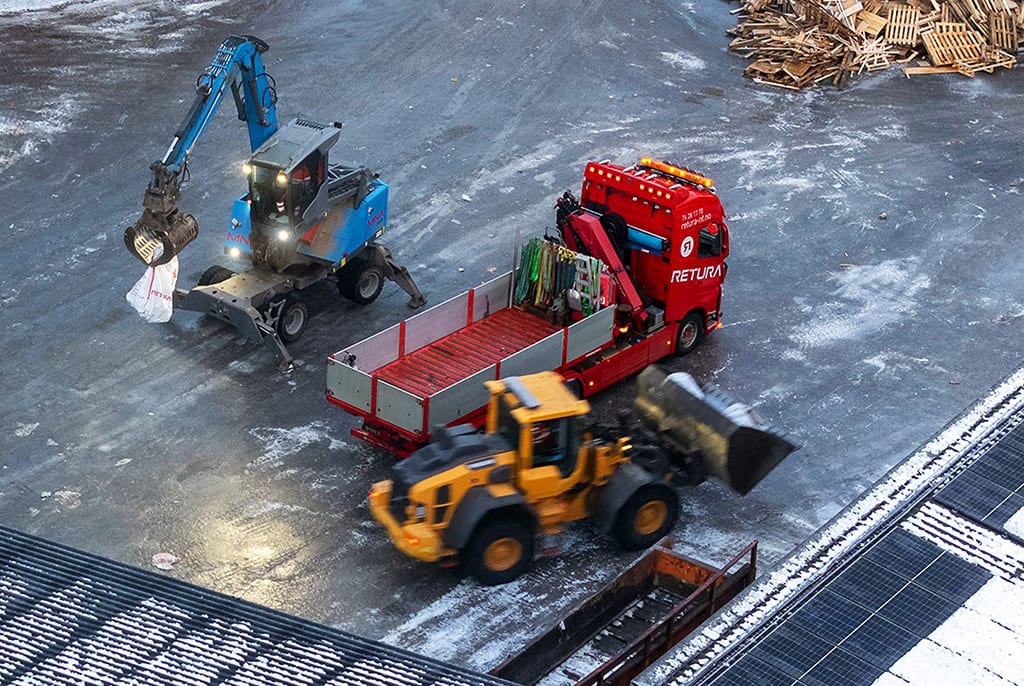 Excavator, truck, and loader moving materials on a snowy industrial site.