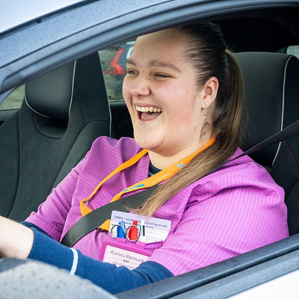 Smiling young woman in purple uniform with ID badge in a car.