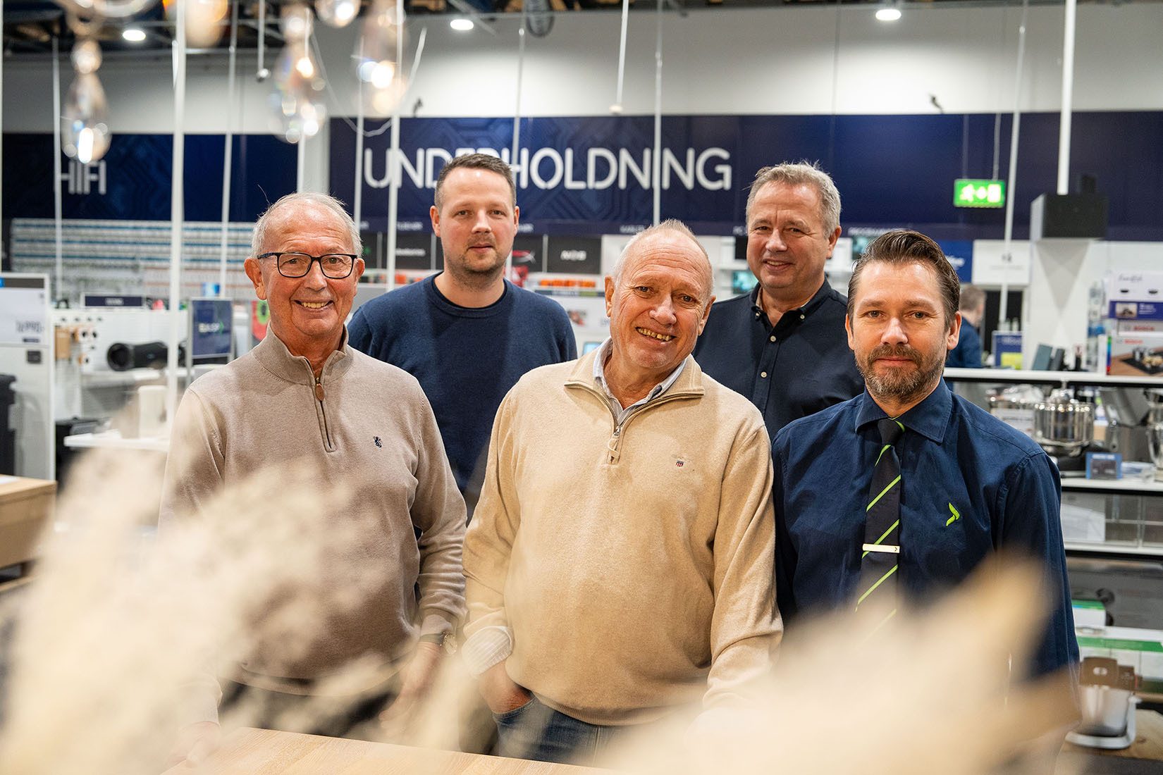 Five men smiling in a store with "HIFI" and "UNDERHOLDNING" signs in the background.