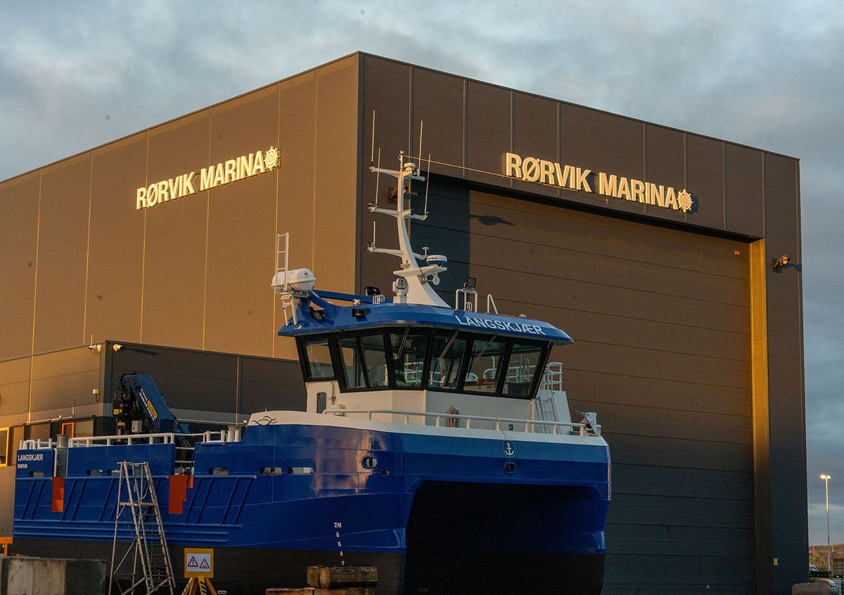 Blue and white boat "LANGSKJÆR" in front of a gray building with "RØRVIK MARINA" signs.