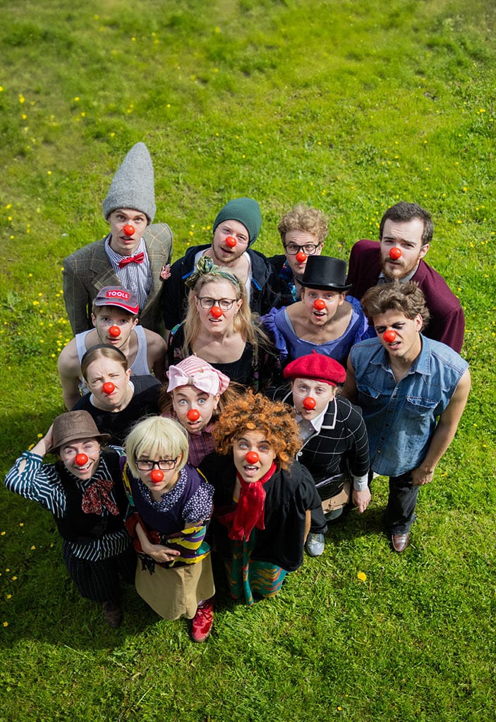 Diverse group with red clown noses looking up from grassy field.
