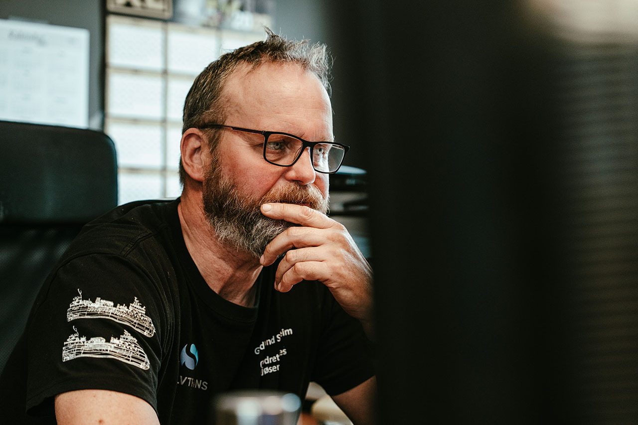 A thoughtful man with a beard and glasses, hand on chin, looking right.