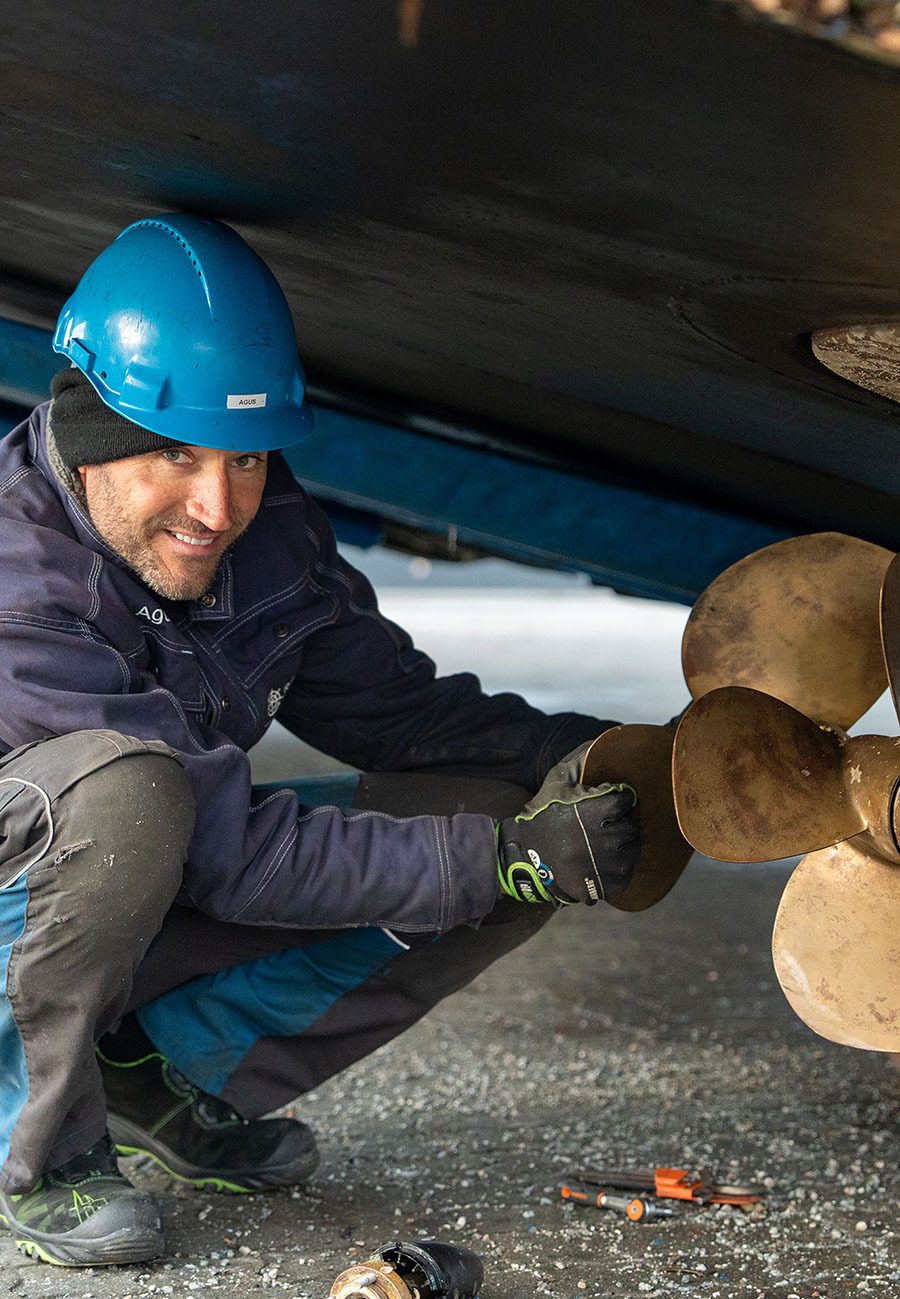 Smiling man in hard hat inspecting a boat's propeller.
