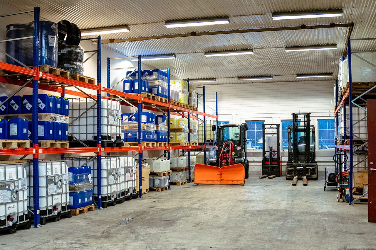 Bright warehouse with tall racks holding blue and white containers, forklifts, and a tractor.