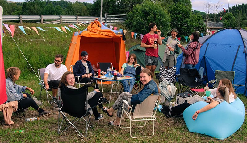 Group of people relaxing around tents at a festival or campsite.