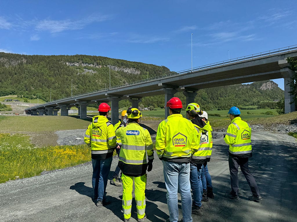 Workers in safety gear inspecting a large concrete bridge construction site outdoors.