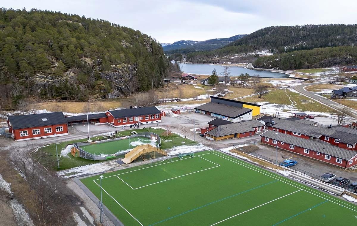 Aerial view of a school campus with multiple red buildings, green sports fields, and a lake in the background.