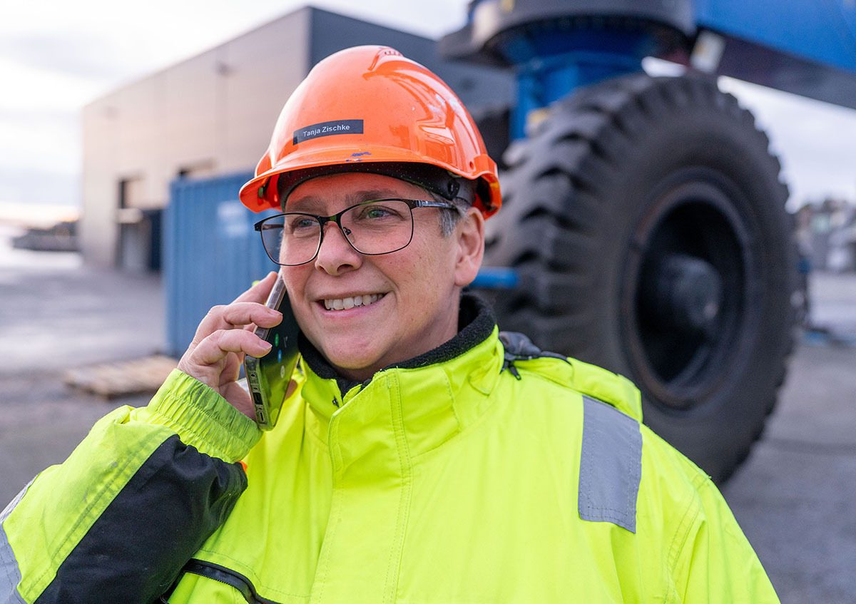 Tanja Zischke, in orange hard hat and hi-vis jacket, smiles while talking on phone.
