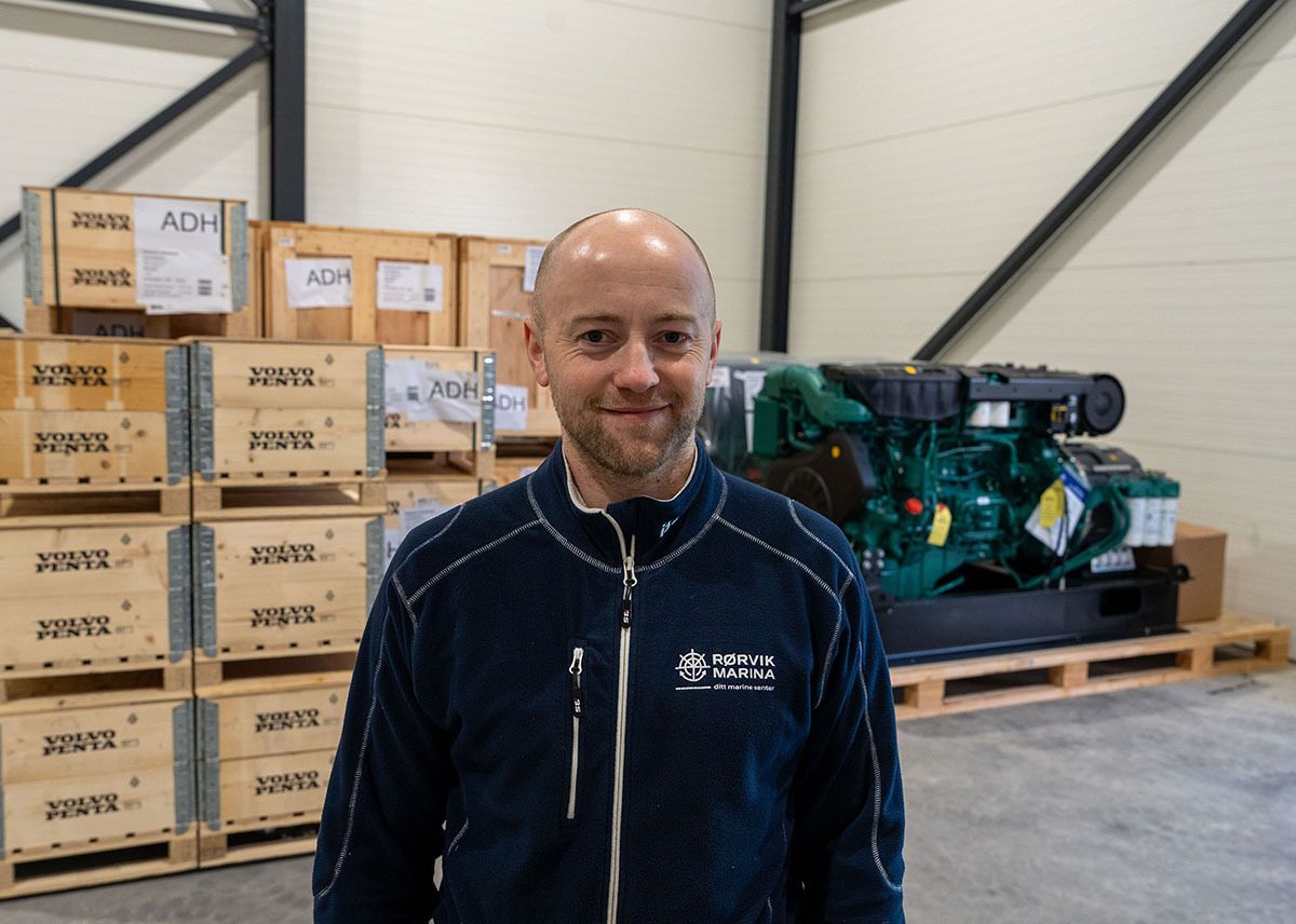 Man in warehouse with Volvo Penta crates and large engine, wearing Rørvik Marina jacket.