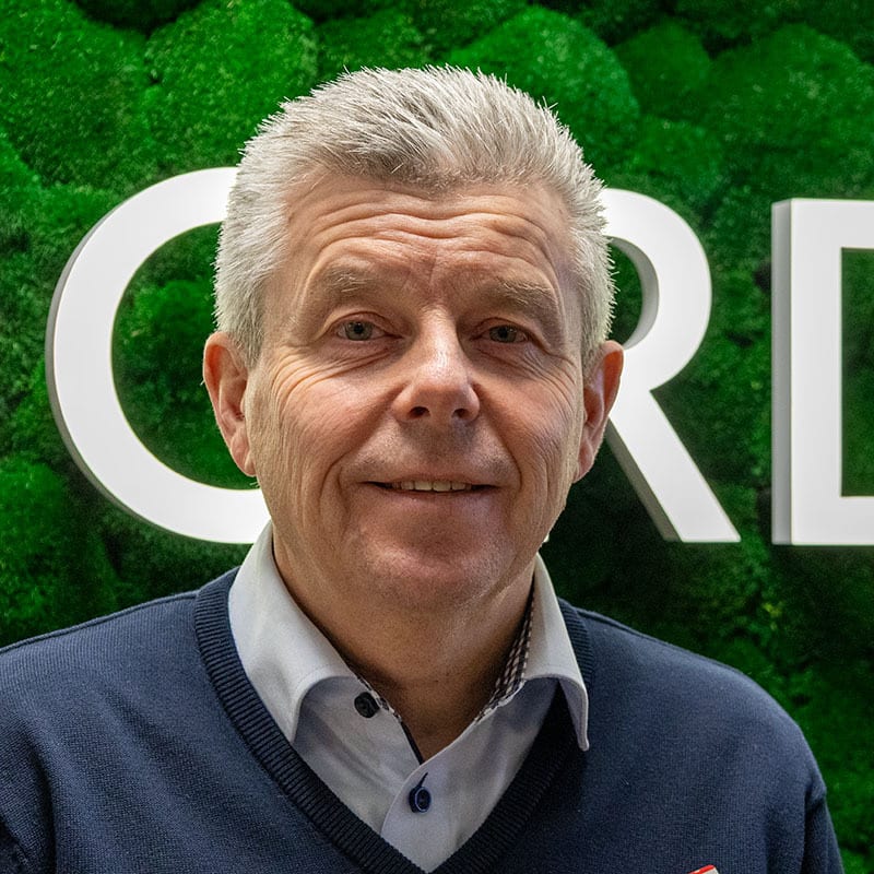 Smiling man with gray hair against green moss wall with letters "C R".