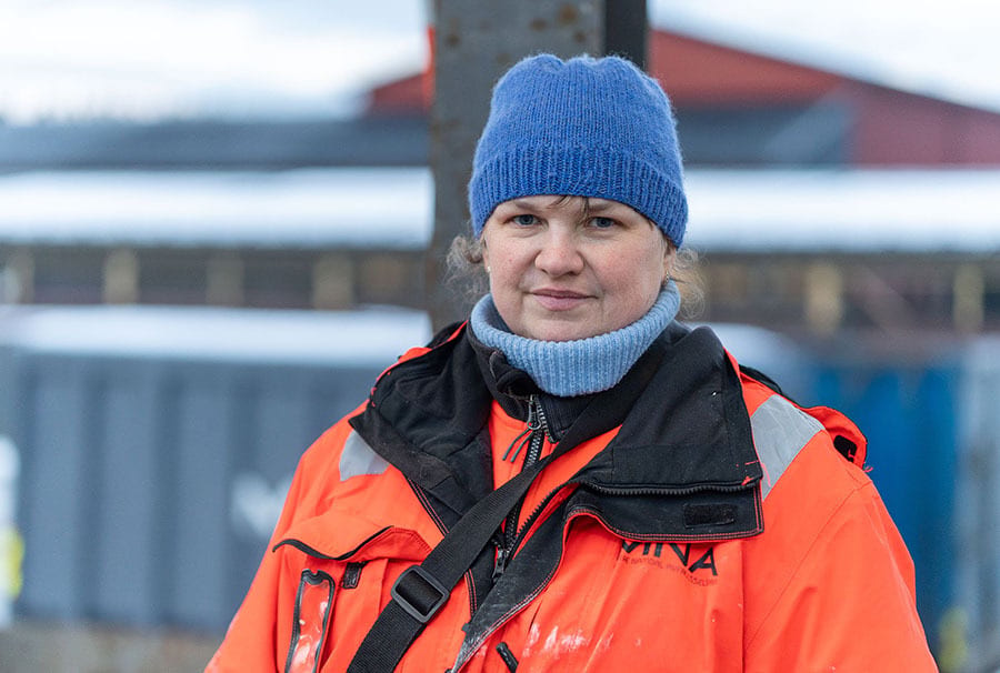 Woman in blue beanie and orange jacket looking at camera outdoors.