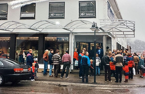 People queuing outside a Telenor store on a rainy day.