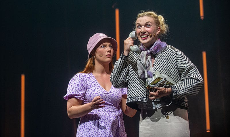 Two women react on stage to a phone call.