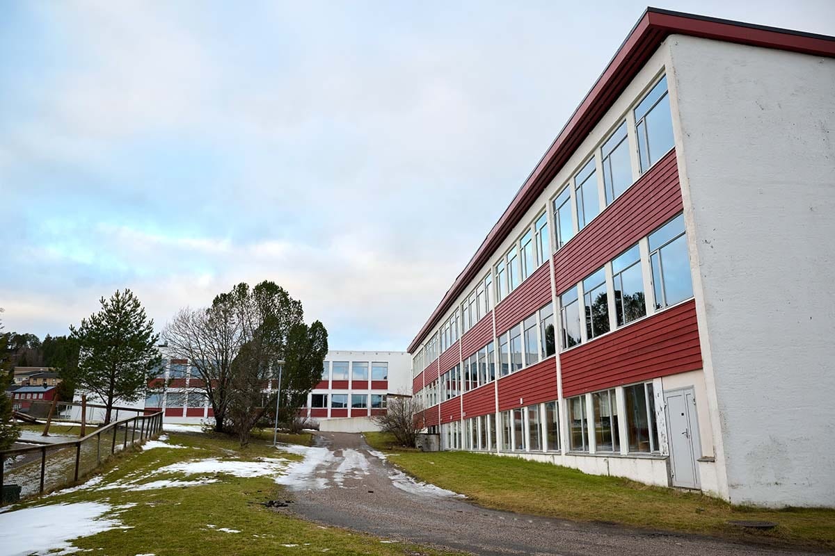 Exterior view of two red and white school buildings with a path, some snow on the ground, and trees.