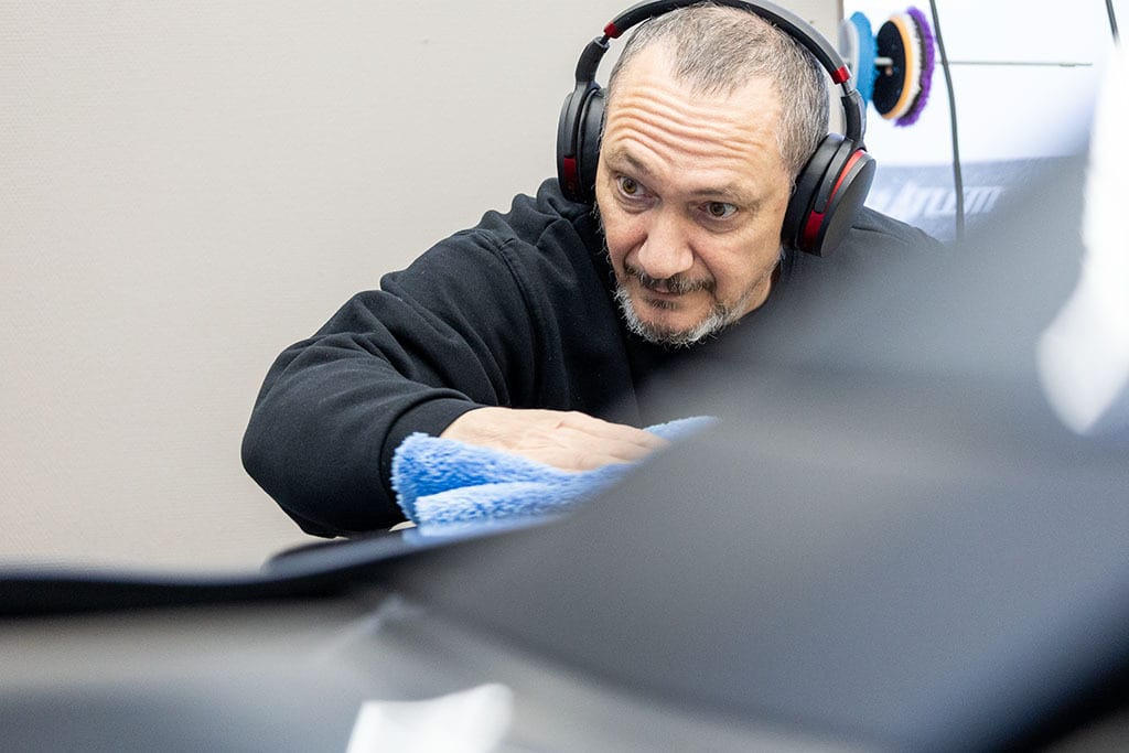 Man in headphones cleaning a dark surface with a blue cloth.