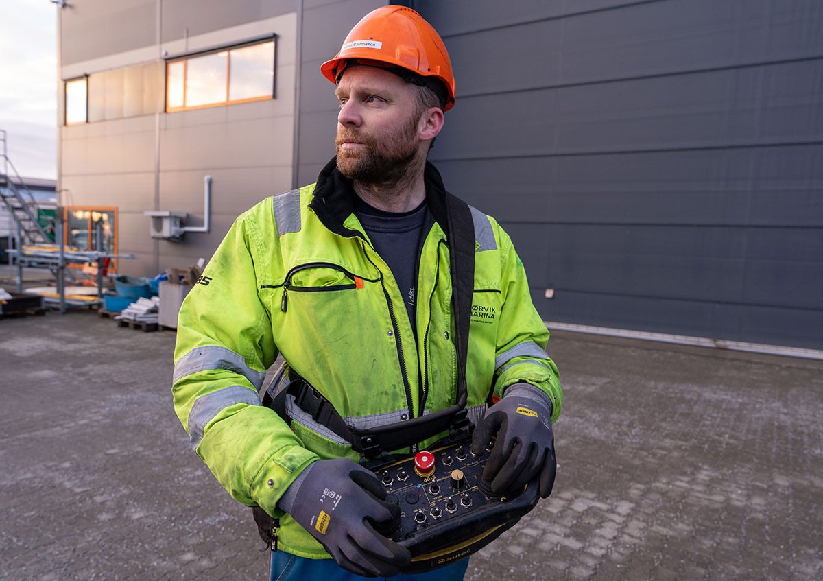Man in hard hat and high-visibility jacket holding a remote control device for machinery.