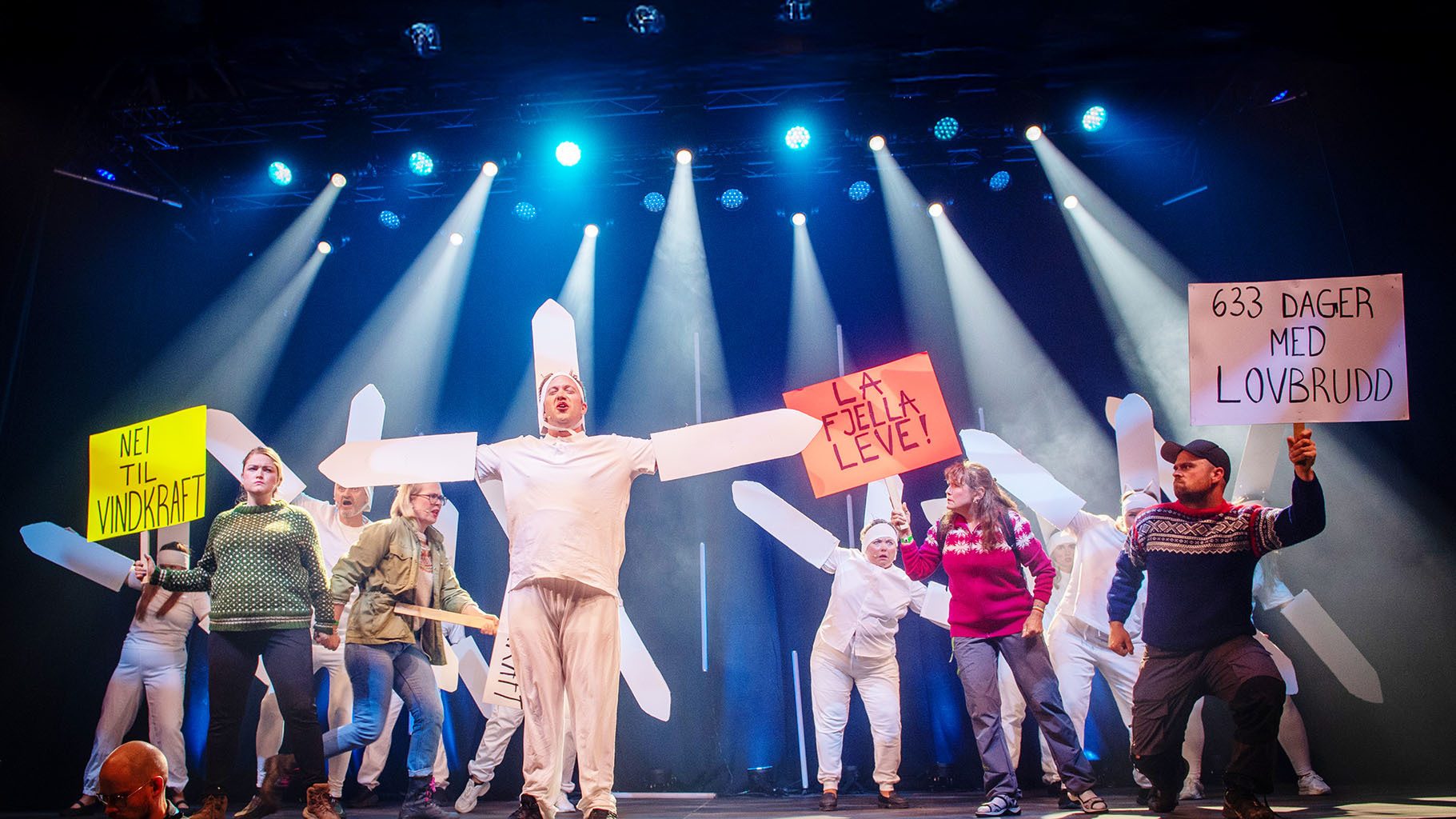 People on stage protesting with signs: "No to Wind Power", "Let Mountains Live", "633 Days Law Breaking".