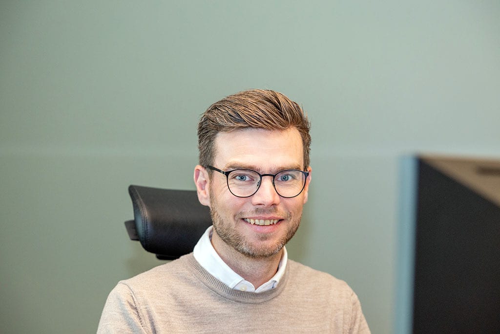 Smiling man in glasses and sweater.